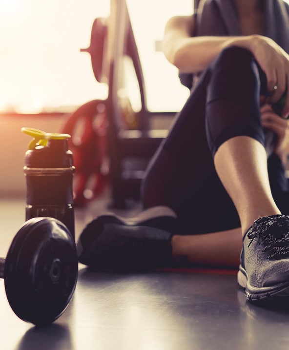 Femme sportive assise au sol après un entraînement, avec un haltère et une bouteille d'eau dans une salle de sport.