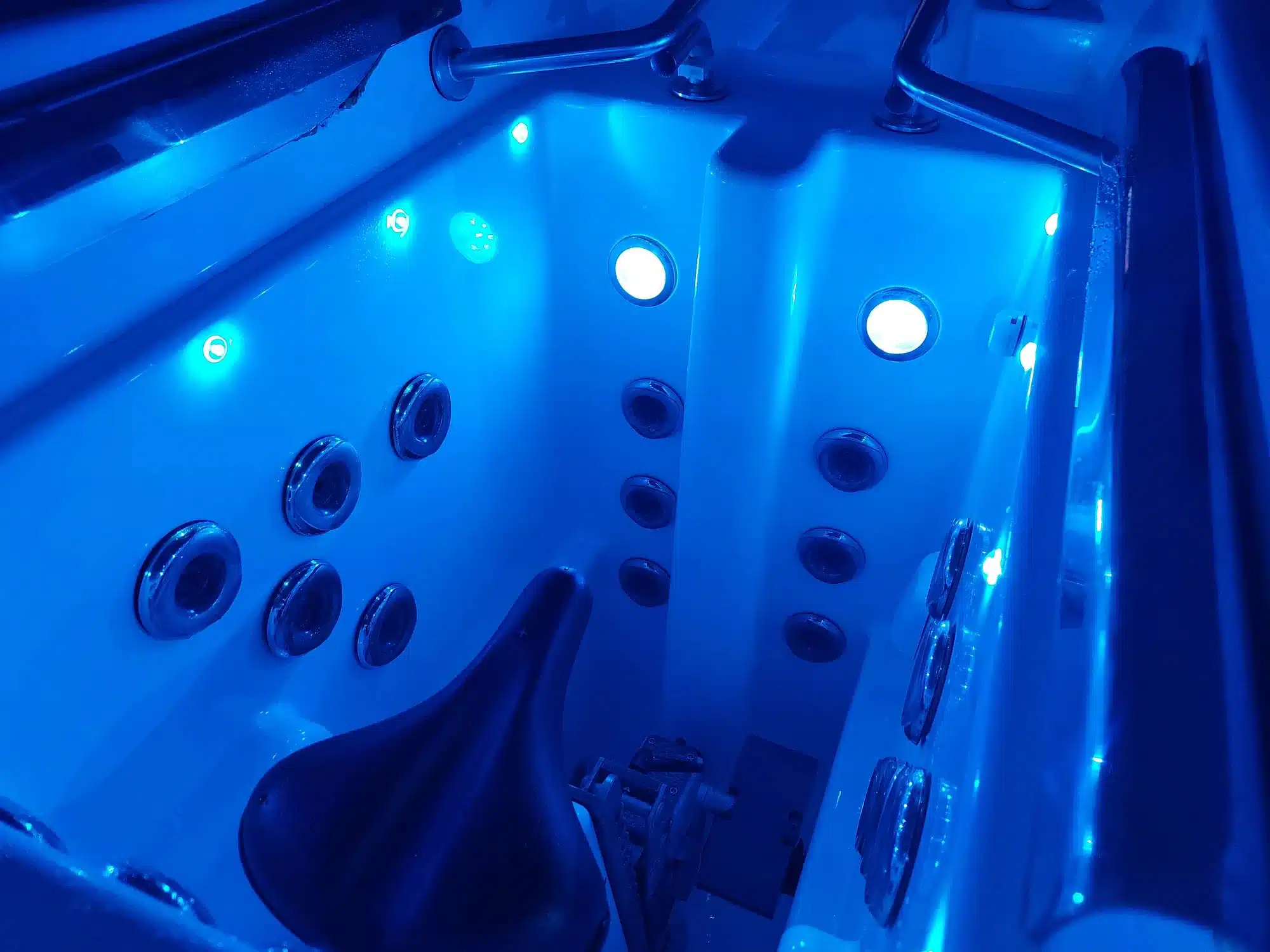 Intérieur bleu lumineux d'un spa de nage avec jets de massage, vélo aquatique intégré et barres de maintien. Idéal pour l'hydrothérapie.